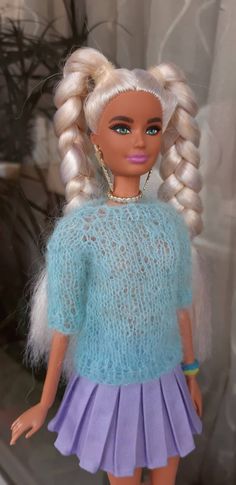 a doll with blonde hair wearing a blue sweater and purple skirt is standing in front of a window