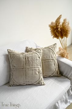 two pillows sitting on top of a white couch next to a vase with dried flowers