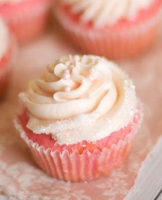 cupcakes with white frosting and sprinkles sitting on a table