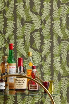 an assortment of liquor bottles on a glass shelf in front of a fern wallpaper