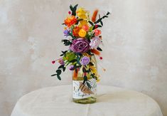 a vase filled with colorful flowers sitting on top of a white cloth covered tablecloth