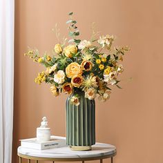 a green vase with yellow and white flowers on a table