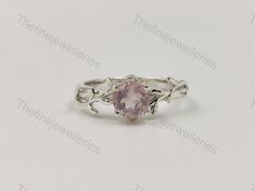 a ring with a pink stone in the center and vines around it, on a white background