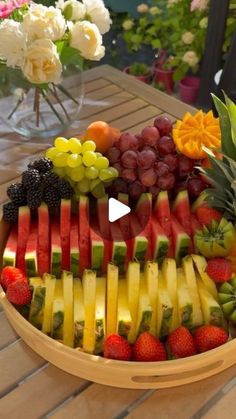 a wooden bowl filled with lots of different types of cut up fruit on top of a table