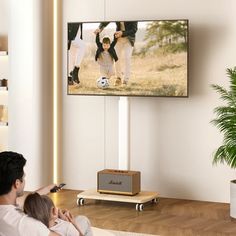 a man sitting in front of a tv holding a baby while watching it on the television