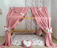 a baby crib with pink drapes and flowers on the top, next to a teddy bear