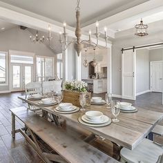 a dining room table with white plates and silverware on it, in the middle of a large open floor plan