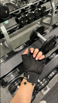 a woman's hand holding onto a pair of black gloves in front of a gym machine