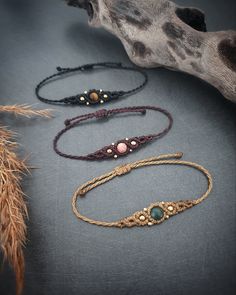 four different bracelets sitting next to each other on a gray surface with a branch in the background