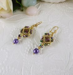 "Woven Crystal Earrings Pearl and Crystal Vitrail These hand woven, sparkling crystal Vitrail chaton stones are encased with permanent finish golden seed beads and two toned crystals featuring a purple pearl drop.  They measure .5\" across and approximately 2\" from the top of the decorative latch back style style ear wires. A beautiful, petite style earring. Design by Cathy Andrews. https://www.etsy.com/shop/IndulgedGirl" Gold Beaded Crystal Earrings, Elegant Purple Beaded Earrings With Faceted Beads, Elegant Purple Round Bead Crystal Earrings, Elegant Purple Crystal Bead Earrings, Elegant Purple Jewelry With Gold Beads, Red Heart Necklace, Petite Style, Purple Pearl, Earrings Pearl