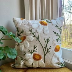 a white pillow sitting on top of a yellow chair next to a green potted plant