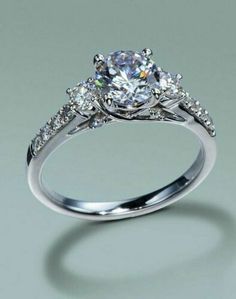 an engagement ring with three stones on the side and one stone in the middle, surrounded by diamonds