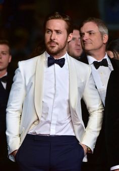 a man in a white tuxedo and bow tie standing next to other men