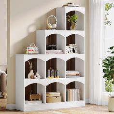 a white book shelf with books on it in a living room next to a potted plant