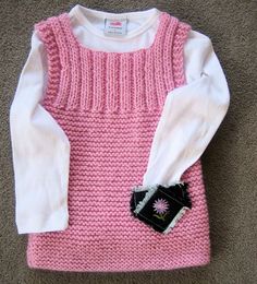 a pink and white sweater is laying on the floor next to a black object in its pocket