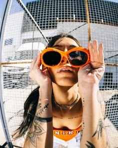 a woman with tattoos and orange sunglasses looking through the hole in front of her face