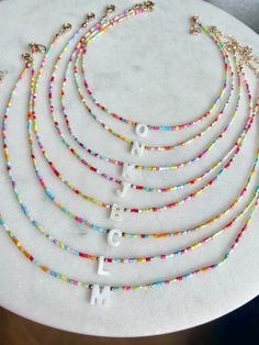 Colourful tiny bead necklaces with adjustable fasteners and Freshwater Pearl initial charm. Perfect for layering with other beaded or chain necklaces at different lengths! Adjustable in length from 16 to 18 inches  Ideal for gifting! Gift packaged in our organza gift bag with business card Personalized Beaded Necklaces For Gifts, Adjustable Round Bead Necklaces For Mother's Day, Personalized Beaded Necklaces With Round Beads, Resizable Beaded Necklaces With Round Beads As Gift, Resizable Beaded Necklace With Round Beads As Gift, Gift Charm Necklaces With Colorful Round Beads, Adjustable White Charm Necklaces With Letter Beads, White Adjustable Charm Necklace With Letter Beads, Multicolor Personalized Dainty Jewelry