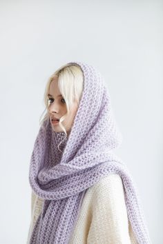 a woman with blonde hair wearing a purple knitted scarf over her head and looking off to the side