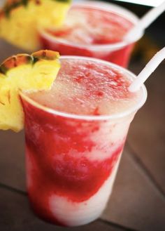 two glasses filled with red and white liquid next to pineapple slices on a table