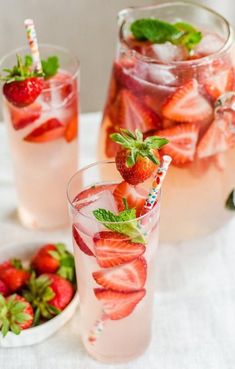 two glasses filled with water and strawberries on top of a white table cloth next to plates