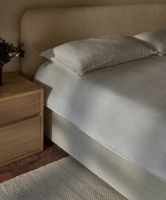 a bed with white sheets and pillows on top of it next to a night stand