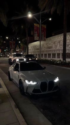 some cars are parked on the side of the road at night in front of palm trees