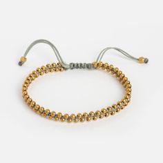 the gold beaded bracelet is shown on a gray string and has an adjustable clasp