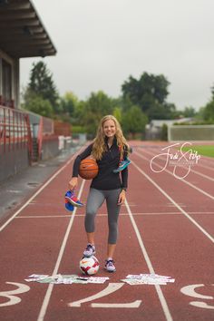 a young woman holding a basketball on top of a red track next to an empty field