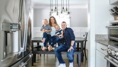 a family sitting on a bench in the middle of a kitchen with stainless steel appliances