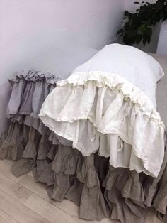 a bed with ruffled sheets and pillows on the floor next to a potted plant