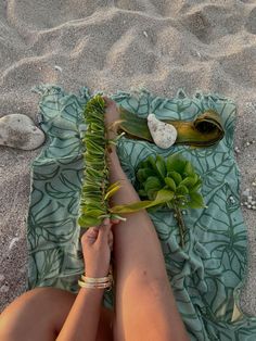 a woman laying on top of a blanket next to a plant and a spoon in the sand