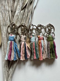 six tasseled key chains hanging from hooks on a piece of driftwood next to a plant