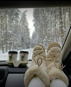 someone's feet in the passenger seat of a car with snow covered trees behind them