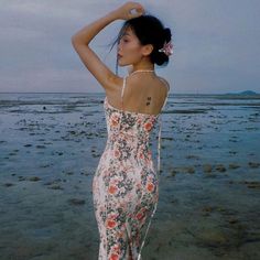 a woman standing in the water with her hand on her head and wearing a floral dress