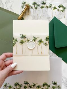 a hand holding an envelope with palm trees on it and a green envelope in the background