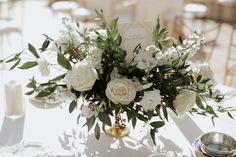 a vase filled with white flowers sitting on top of a table next to silver dishes