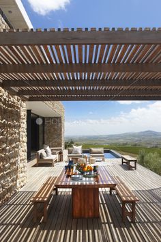 a wooden table sitting on top of a wooden deck next to a stone wall and covered patio