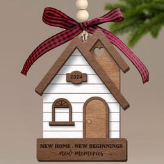 a wooden house ornament with a red ribbon on it's top and the words new home, new beginnings next merry