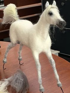 a white horse standing on top of a wooden table next to a ball of yarn