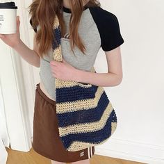 a woman is holding a coffee cup and wearing a crocheted bag with stripes on it