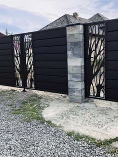 a black gate with trees on it in the middle of graveled area next to a building