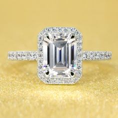 an emerald cut diamond ring with pave set diamonds surrounding the band on a gold background