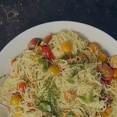 a white bowl filled with pasta and vegetables on top of a black countertop next to a fork