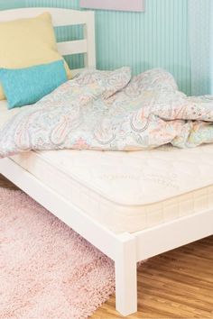 an unmade bed in a bedroom with blue walls and pink rugs on the floor