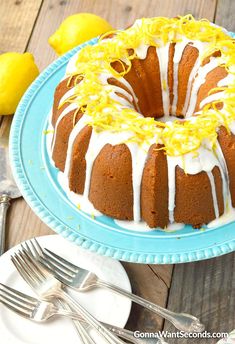 a bundt cake with lemons and icing on a blue plate next to silverware