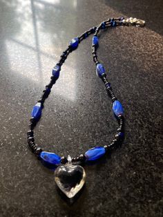 Black heart charm with blue accent beads and black and blue seed beads neckless. Approximately 19 inches. Blue Heart-shaped Jewelry With Colorful Beads, Blue Heart Beaded Necklaces, Blue Beaded Heart Pendant Jewelry, Blue Handmade Beaded Necklaces With Heart Pendant, Handmade Blue Beaded Necklaces With Heart Pendant, Handmade Blue Beaded Necklace With Heart Pendant, Blue Necklace With Black Beads For Gift, Blue Heart Beads Heart-shaped Necklace, Blue Beaded Necklace With Heart Pendant