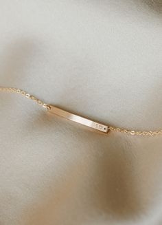 a thin gold bar bracelet on a white fabric background with the word love written across it