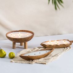 two wooden bowls sitting on top of a table next to pears and candle holders