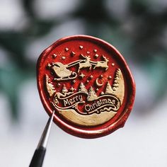 a red wax stamp with santa claus and reindeers in the sky on it, holding a pair of scissors