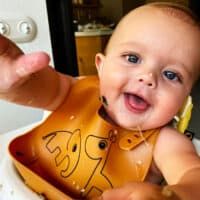 a baby is sitting in a high chair with his bib on and smiling at the camera